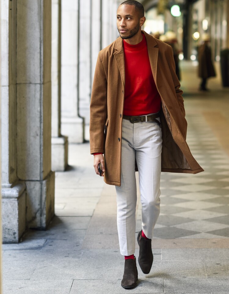 Fashionable young man wearing red, pullover and brown coat walking along arcade